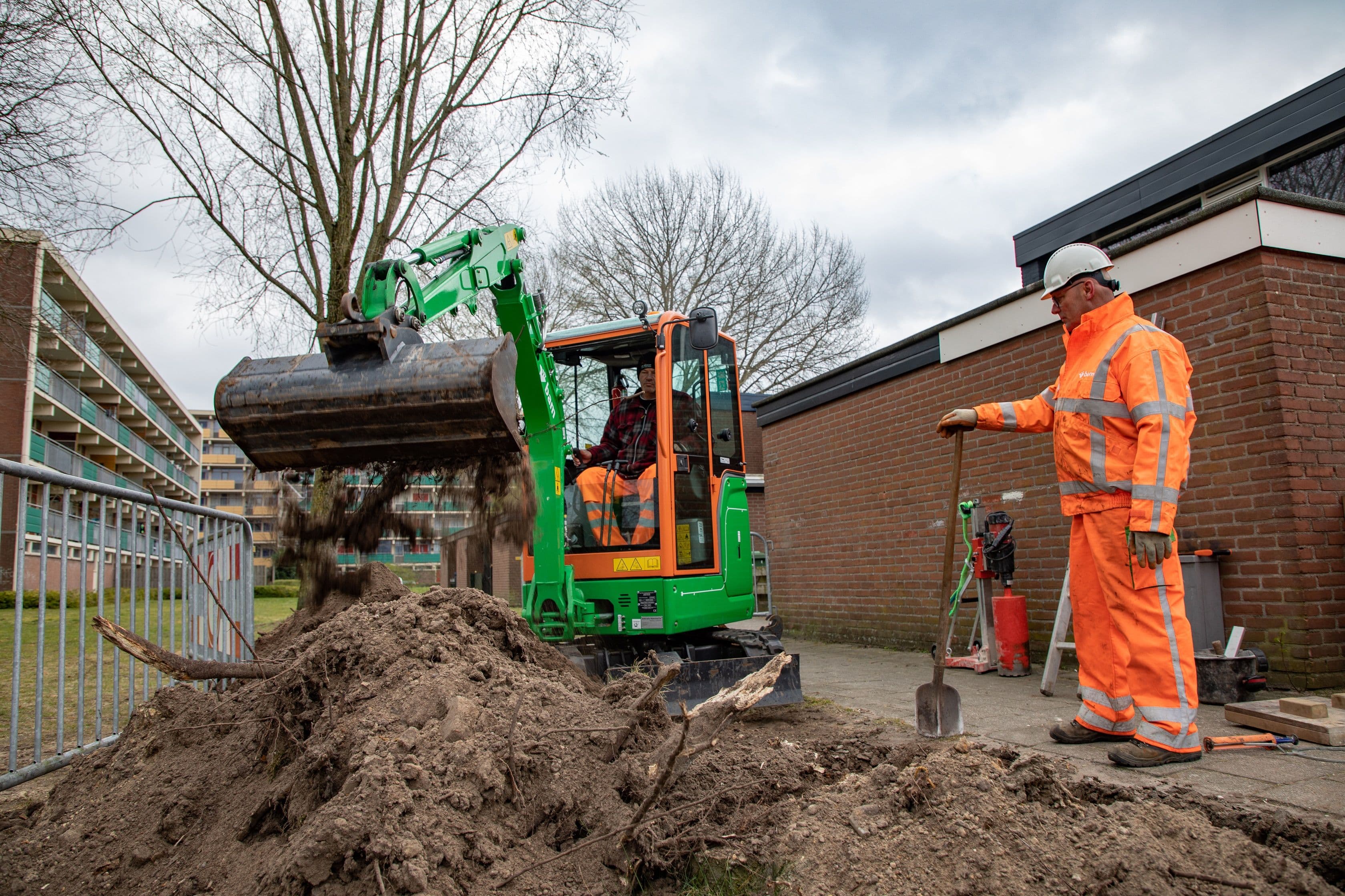 graafmachine aan het werk met een man in een oranje outfit met een schep ernaast